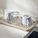 Tørremåtte under opvaskestativ med kopper og glas.