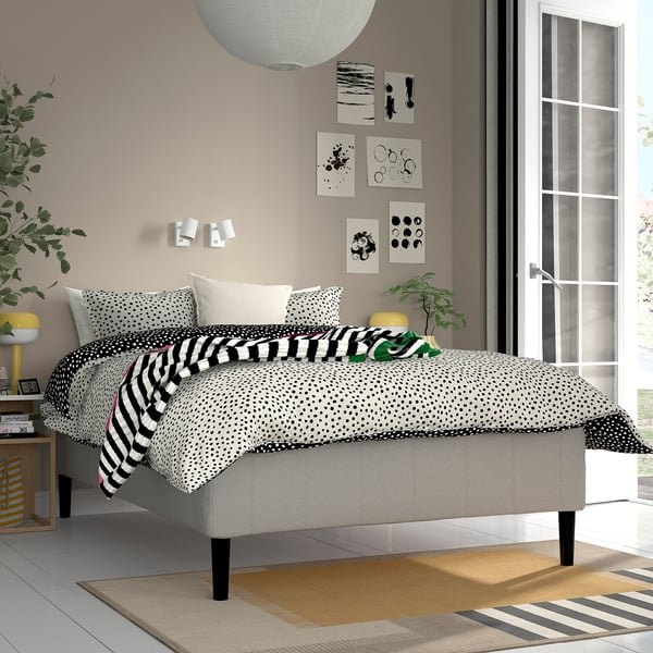 Moderne soveværelse med prikket seng, stribet plaid, abstrakt kunst, grå polstret sengeramme, natbord, gul lampe og mønstret tæppe.