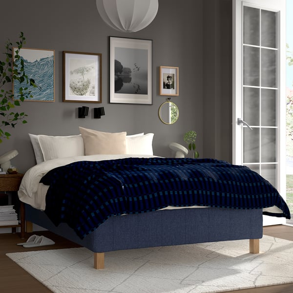 Moderne soveværelse med RISHÖJDEN seng, mørkeblå dyne, hvide og beige puder. Grå vægge, kunst, spejl, stort vindue, lyst tæppe.