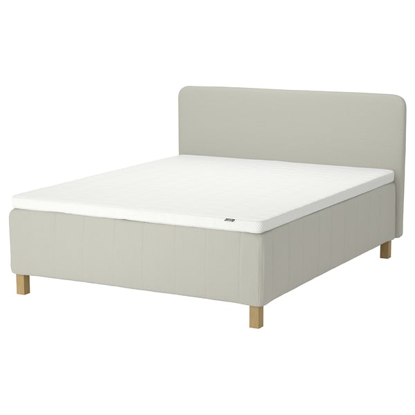 En beige RISHÖJDEN seng med polstret sengegavl, træben og hvid madras. Det er et moderne, minimalistisk design til et hyggeligt soveværelse.