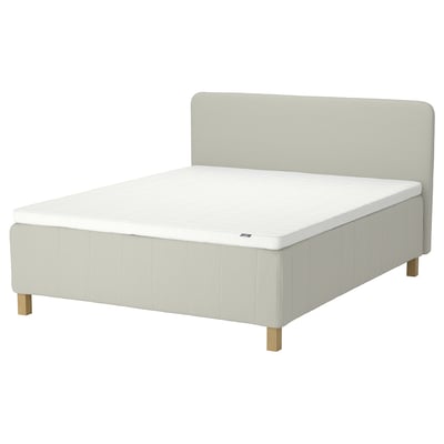 En RISHÖJDEN seng i beige. Den har et polstret hovedgærde, træben og en hvid madras.
