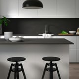 Moderne sort køkken med porcelænsbord og vask, taburetter og pendel.