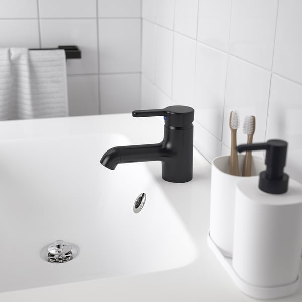 En moderne håndvask på badeværelset med et slankt sort SALJEN armatur, hvid bordplade og en tandbørsteholder.