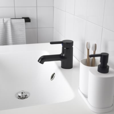 En moderne håndvask på badeværelset med et slankt sort SALJEN armatur, hvid bordplade og en tandbørsteholder.
