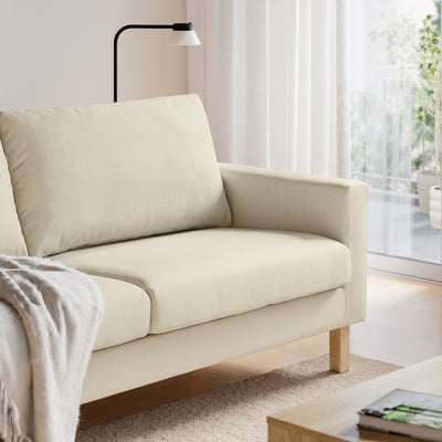 En beige stofsofa, der giver et hyggeligt og behageligt siddeområde med lette træben, stilfuldt placeret i en stue.