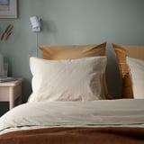 Hyggeligt soveværelse med store brune velour SANELA puder, beige sengetøj og minimalistisk natbord med lampe.