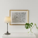 Minimalistisk opholdsrum med billetstempelcollage, lampe og plante.