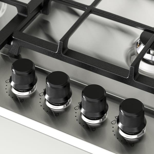 Fire knapper på et gaskomfur, sort med metallisk bund, justeret på et sølv kontrolpanel, hvilket indikerer design og funktionalitet af høj kvalitet.