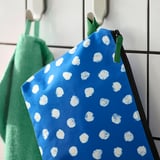 Blå toilettaske med hvide prikker hænger i en krog med en grøn lynlås og rum til organisering.