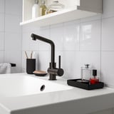 Lille sort SKOGSVIKEN badeværelsesarrangør sidder ved siden af håndvasken med toiletartikler og makeup.
