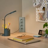 Træskrivebord med grøn SKOPAT-ledning, bærbar computer, notesbøger, hovedtelefoner og en plante.