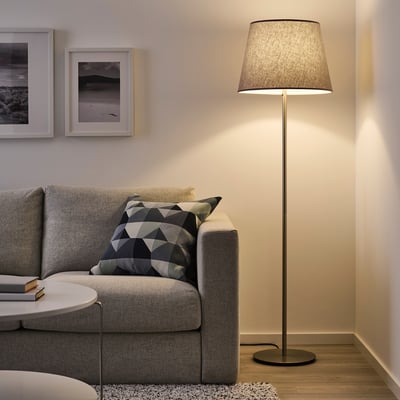 Skottor gulvlampe ved siden af grå sofa, med delvis skyggebelysning, der tilføjer hyggelig stemning. Dens slanke design komplementerer moderne stuer.