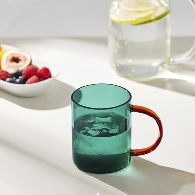 Teal iskrus med orange håndtag på lyst bord ved frugt.