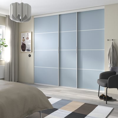 Moderne soveværelse med lyseblå skydedøre, et gråt tæppe og en beige dyne på sengen.