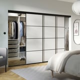 Moderne soveværelse med store, minimalistiske hvide og sorte skabe, der indeholder organiseret tøj og tilbehør.