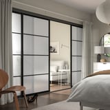 Moderne soveværelse: SKYTTA glasskabslåger, sorte rammer, grå gardiner, træmøbler, hvidt sengetøj, træstol, matterede paneler.
