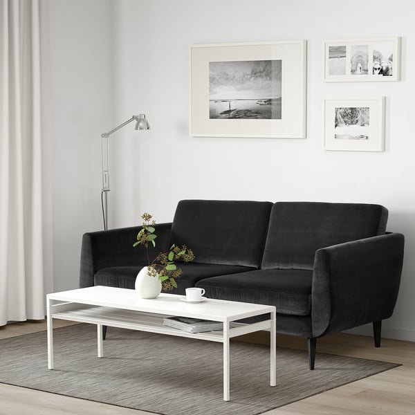 Sofa, sofabord, gulvlampe i stuen. Sort sofa, hvid indretning.