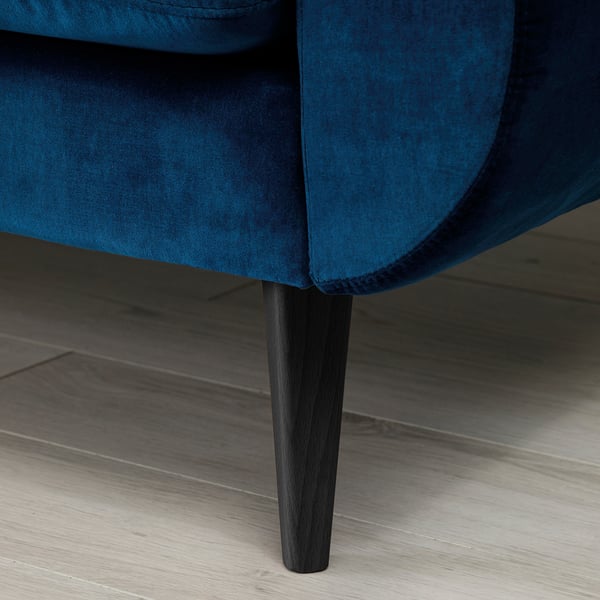 Blå fløjlssofa med slanke, mørke træben, der viser moderne og stilfuldt design.