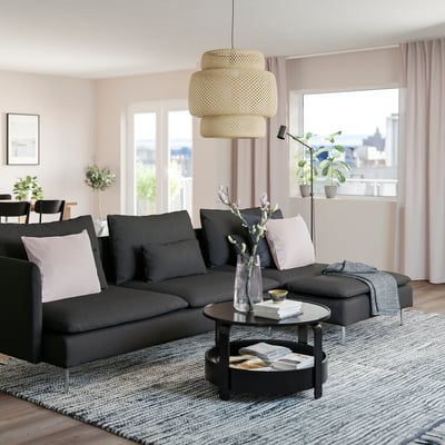 Moderne sort SÖDERHAMN sofa med høje ben og dybe sæder. Stort parti med puder, under en hængende gul lampe.