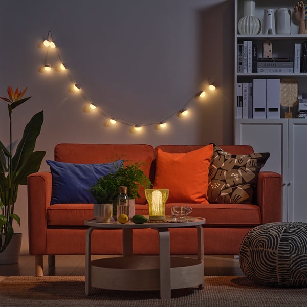 Hyggelig stue med orange sofa, lyskæder, sofabord og bogreol.