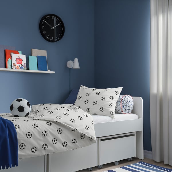 Børneblå værelse med fodboldsengetøj, legetøj, bøger, ur, lampe, gardin.