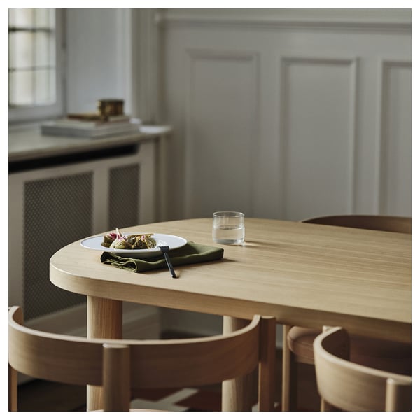 Moderne spisestue med lyst træbord, tallerken, glas, serviet nær køkken.