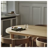 Moderne spisestue med lyst træbord, tallerken, glas, serviet nær køkken.