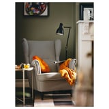 Hyggeligt hjørne med STRANDMON hundetandslænestol, orange hynder, gult tæppe, gulvlampe og grønne vægge.