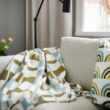 Et gulgrønt og gråturkis tæppe af genanvendt polyester på en sofa, der komplementerer geometriske puder.