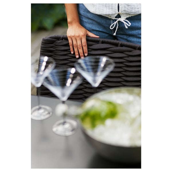 En person, der håndterer sorte vævede dækkeservietter ved siden af klare glas på et bord.