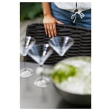 En person, der håndterer sorte vævede dækkeservietter ved siden af klare glas på et bord.
