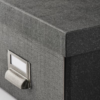 En TJOG opbevaringsboks i mørkegrå med en metaletiketholder på den ene side. Den er rektangulær og lavet af genbrugspap.