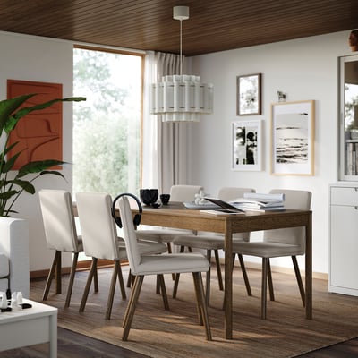 Moderne spisestue med træbord og 6 stole, hvid indretning, bøger, plante, stort vindue, kunst og stilfuldt lysarmatur.