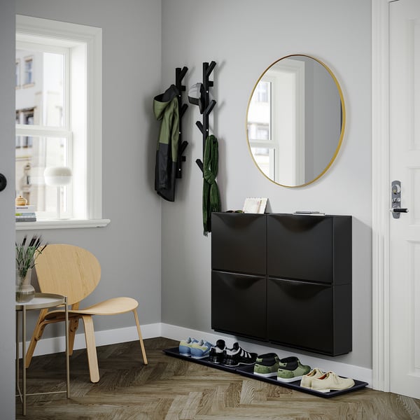 Sort moderne skoskab, TRONES fra ikea, med et rundt guldspejl og træbøjlestativ.