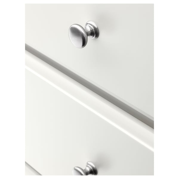 Nærbillede af hvid kommode med metalliske knopper, der viser glatte, blødtlukkende skuffer og polerede kanter.
