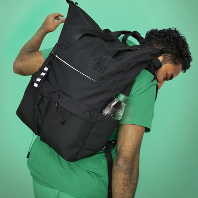 Person med stor sort rygsæk af genanvendt polyester, flere rum, polstrede stropper, sidelommer, stribet nøglering.