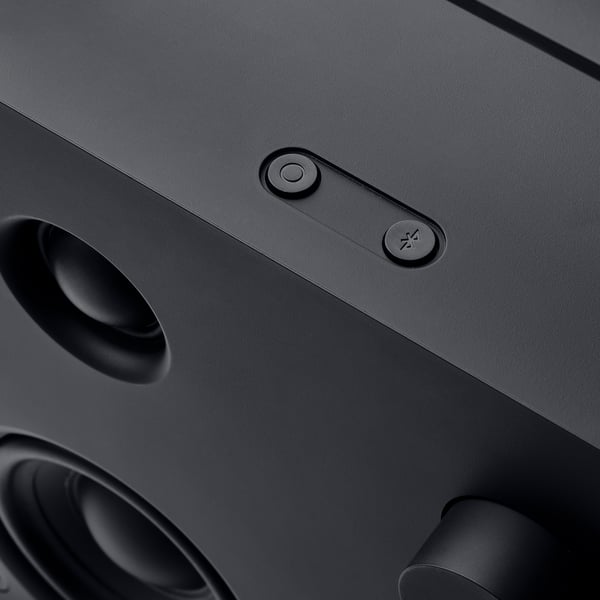 Nærbillede af en slank sort bluetooth-højttaler med en cirkulær lydstyrkeknap og et Bluetooth-forbindelsesikon, der viser et moderne design.