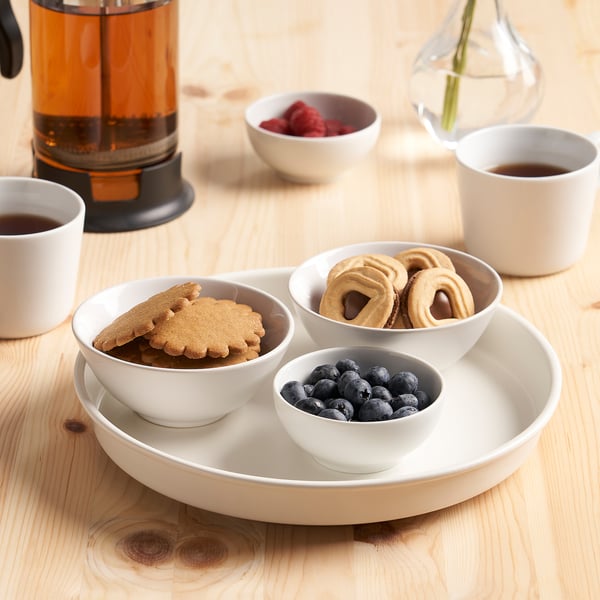 Et køkkenbord med småkager, bær og kaffe i kopper omkring en roterende drejeskive med flere snacks.