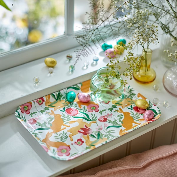 Påsketema bakke med blomsterdekorationer og chokoladeæg; inkluderer dekorative vaser og blomster på en vindueskarm.