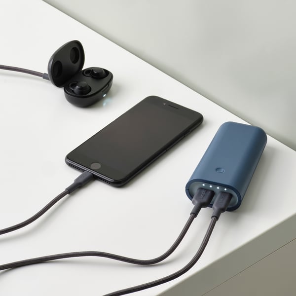 Billedet viser en telefon og trådløse øretelefoner, der oplades samtidigt fra en blå powerbank med to porte.