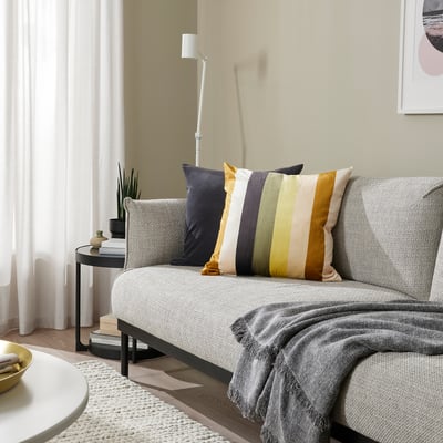 Moderne stue med VATTENVÄN sofa, pyntepuder, sofabord, lampe og tæppe. Lys med naturligt lys og gennemsigtige gardiner.