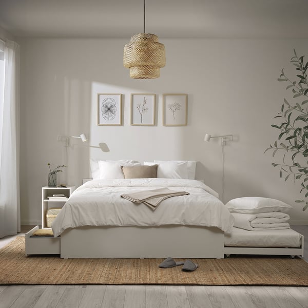 Minimalistisk hvidt sengesæt med matchende opbevaringskasser og hængende lampe. To kunstrammer ovenfor.