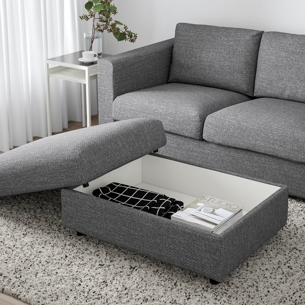 Moderne stue med en grå VIMLE sofa og skammel. Skammelen har et hæveligt sæde, der afslører opbevaringsplads med bøger og en fjernbetjening indeni.
