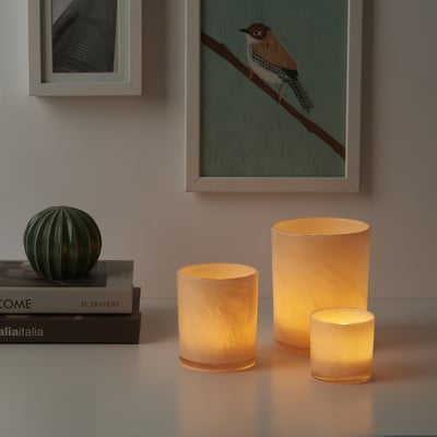 Tre glødende VINDSTILLA lysestager med unikke mønstre ved siden af bøger.