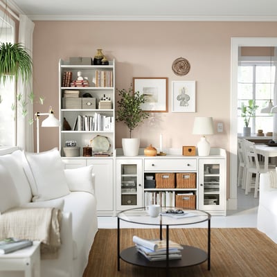 Lys stue med VITTSJÖ sofabord. Hvid sofa, glasbord, bogreol med indretning. Naturligt lys, potteplanter.