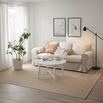 Moderne stue med beige tæppe, sofa, sofabord, lampe, plante og billeder.