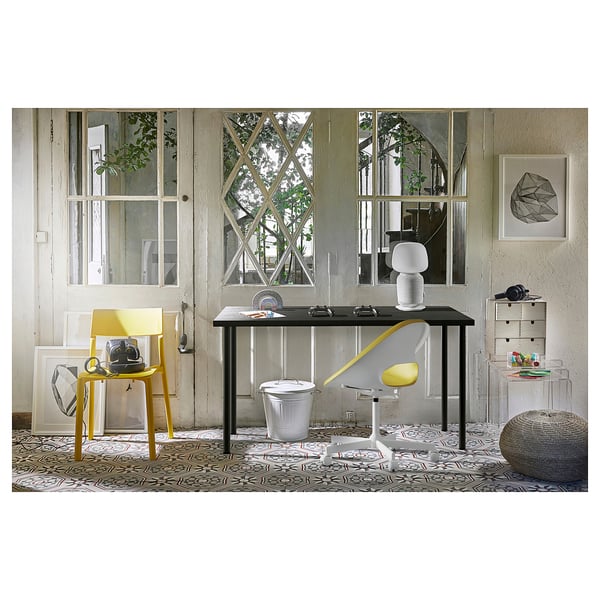 Modern home office with ADILS desk, featuring yellow and white chairs, patterned rug, and large window.