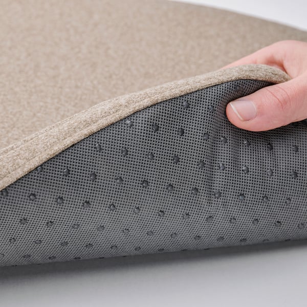 Hand lifts edge of ÄLVGRÄSMAL cushion, showing water-resistant mesh underside with anti-slip dots.