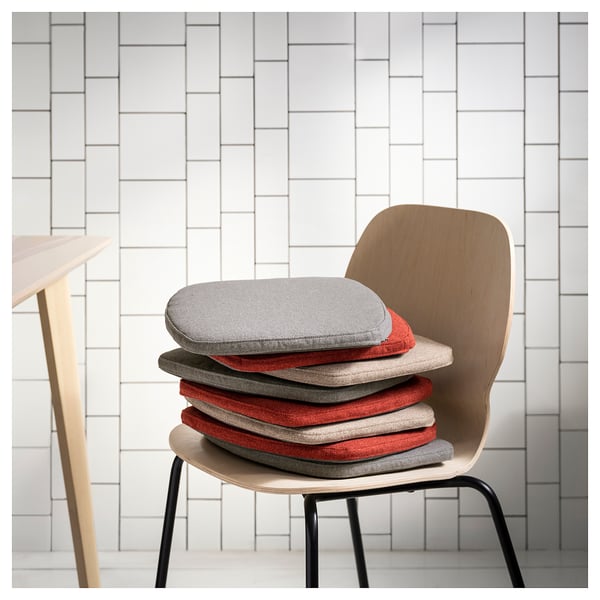 Modern dining chair with stack of round cushion pads in grey, red, and beige colors, leaning against a white brick wall.