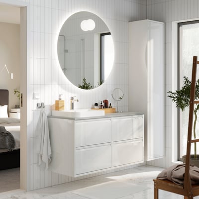 Modern white bathroom with glossy ÄNGSJÖN vanity, round mirror, & potted plant.